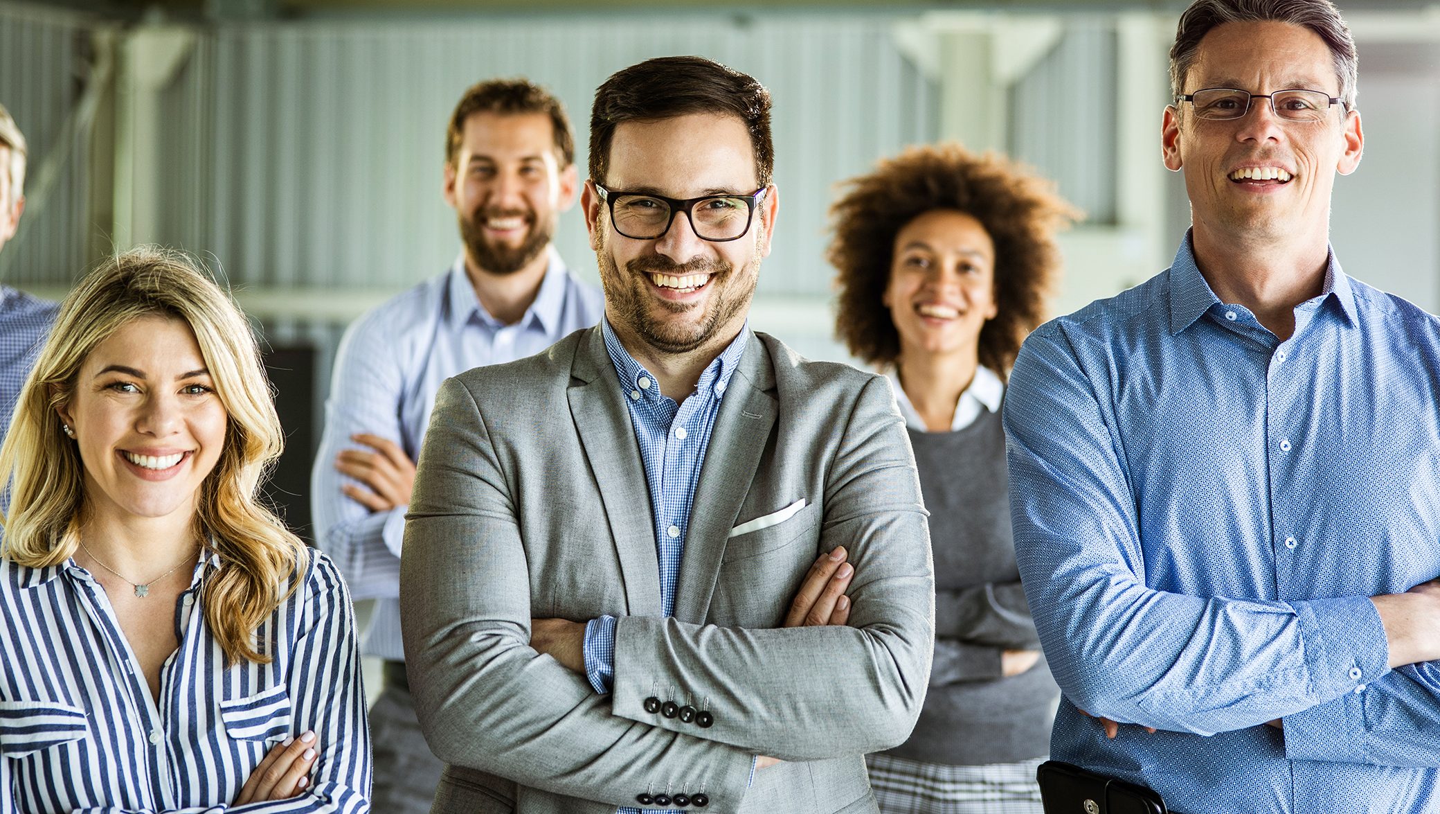 Panoramic view of large group of happy entrepreneurs standing in the office with crossed arms and looking at camera.
