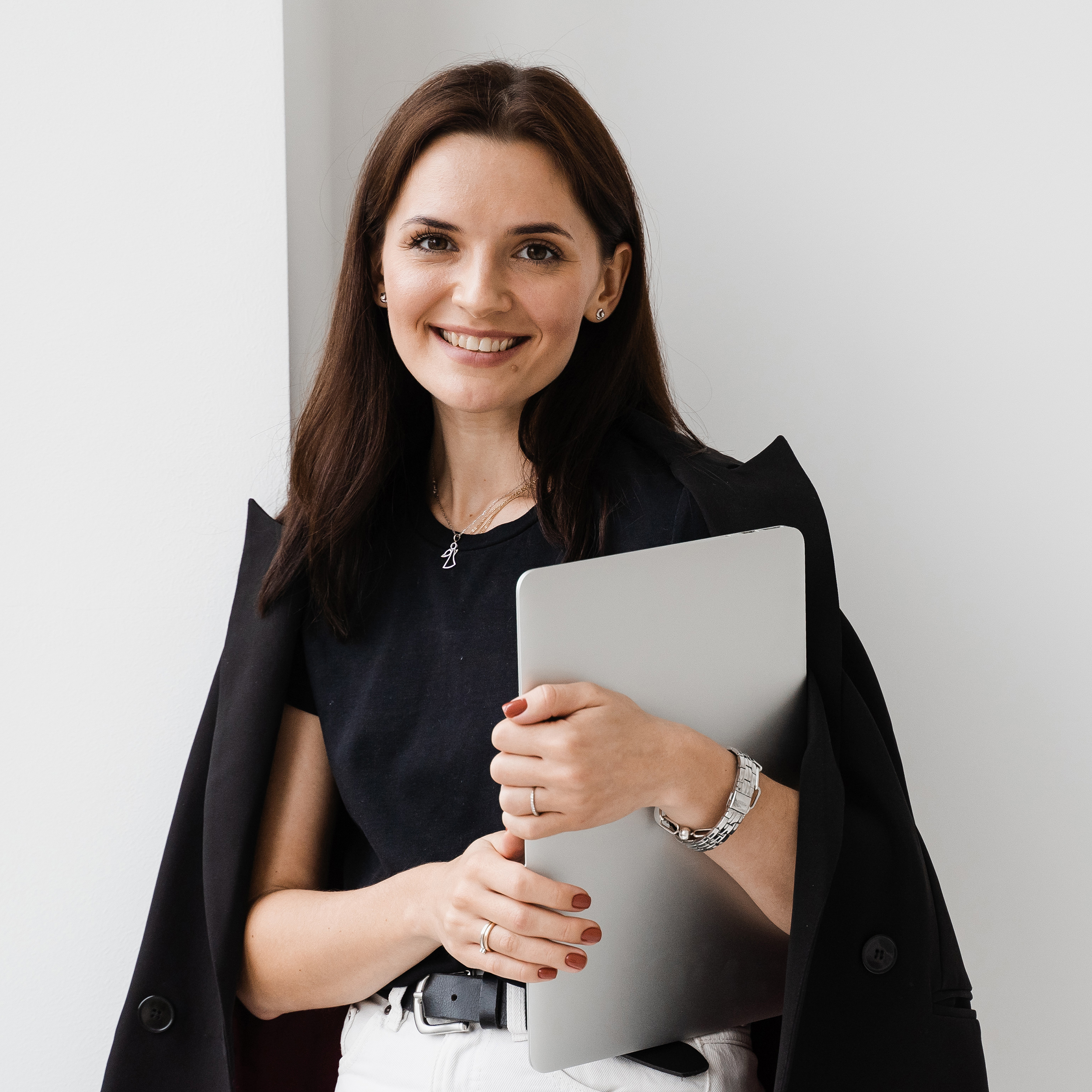 Young woman is hugging her laptop and smiling in cafe. Cheerful girl with laptop standing near big window in the white office